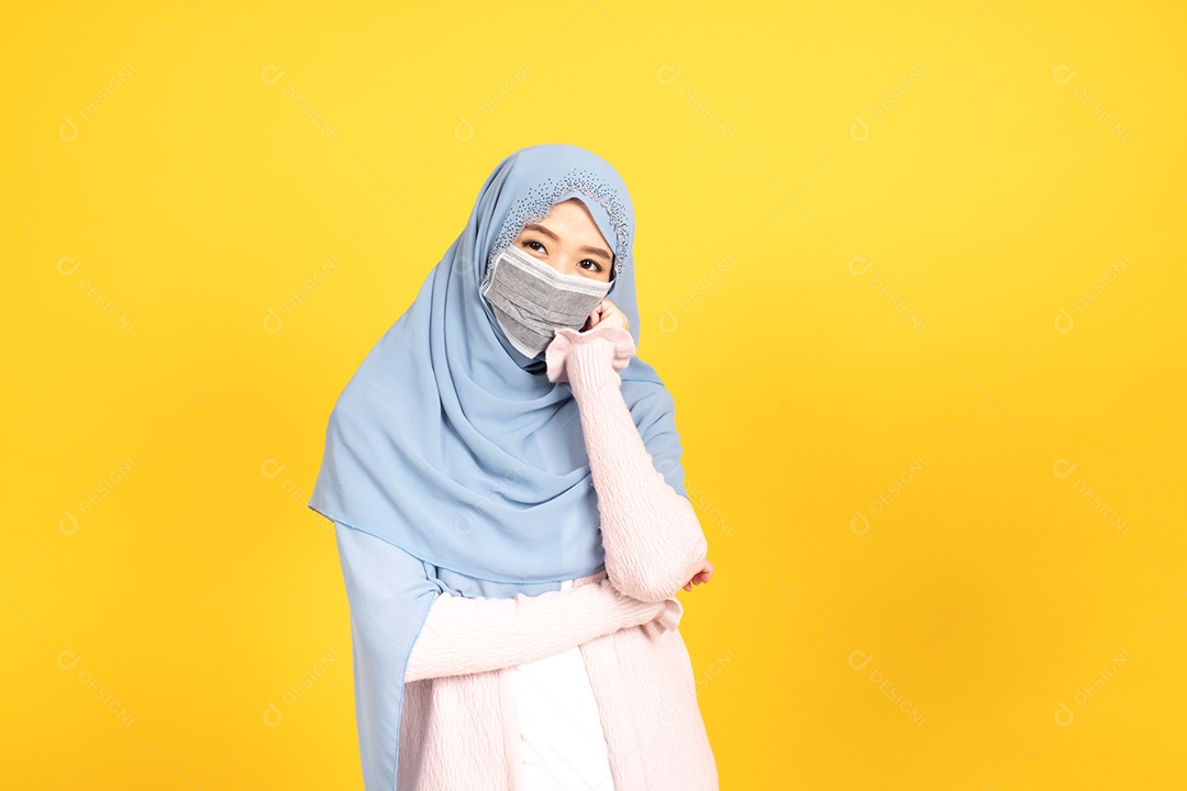 Retrato de menina muçulmana asiática em hijab usando máscara facial no estúdio amarelo.