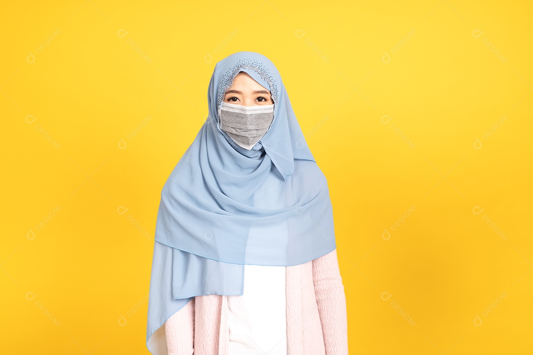 Retrato de menina muçulmana asiática em hijab usando máscara facial no estúdio amarelo.