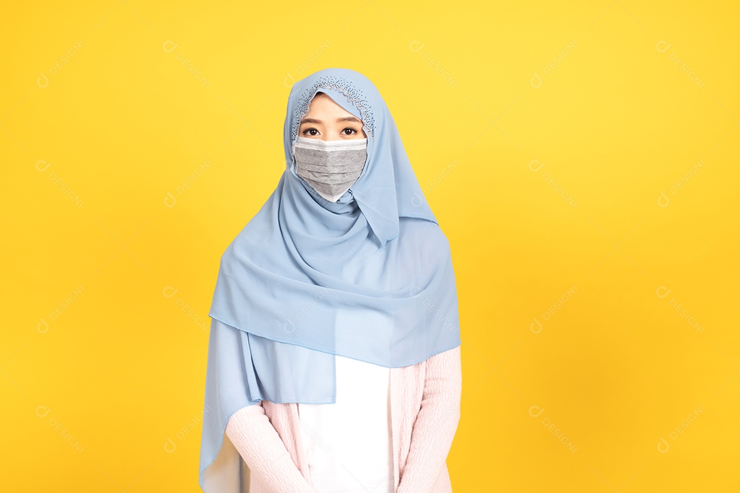 Retrato de menina muçulmana asiática em hijab usando máscara facial no estúdio amarelo.