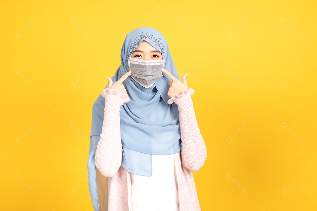 Retrato de menina muçulmana asiática em hijab usando máscara facial no estúdio amarelo.