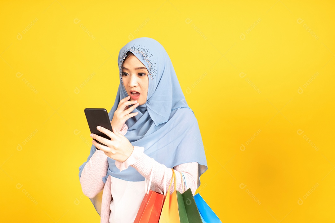 Jovem religiosa árabe sorridente usa hijab de véu segura sacola de compras sobre fundo amarelo.