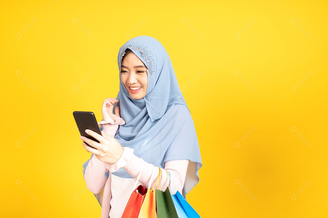 Jovem religiosa árabe sorridente usa hijab de véu segura sacola de compras sobre fundo amarelo.