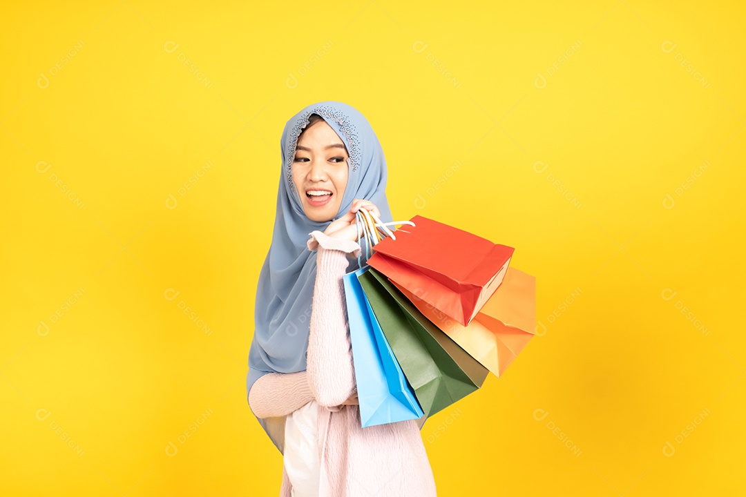Jovem religiosa árabe sorridente usa hijab de véu segura sacola de compras sobre fundo amarelo.