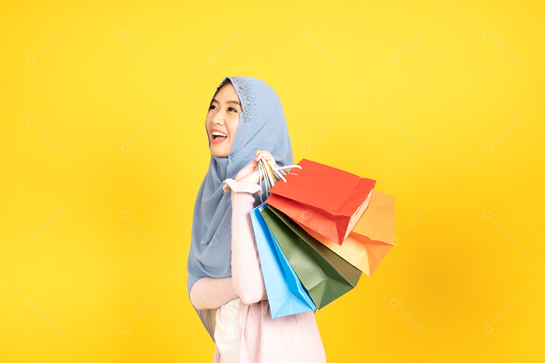 Jovem religiosa árabe sorridente usa hijab de véu segura sacola de compras sobre fundo amarelo.
