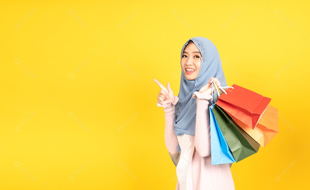 Jovem religiosa árabe sorridente usa hijab de véu segura sacola de compras sobre fundo amarelo.
