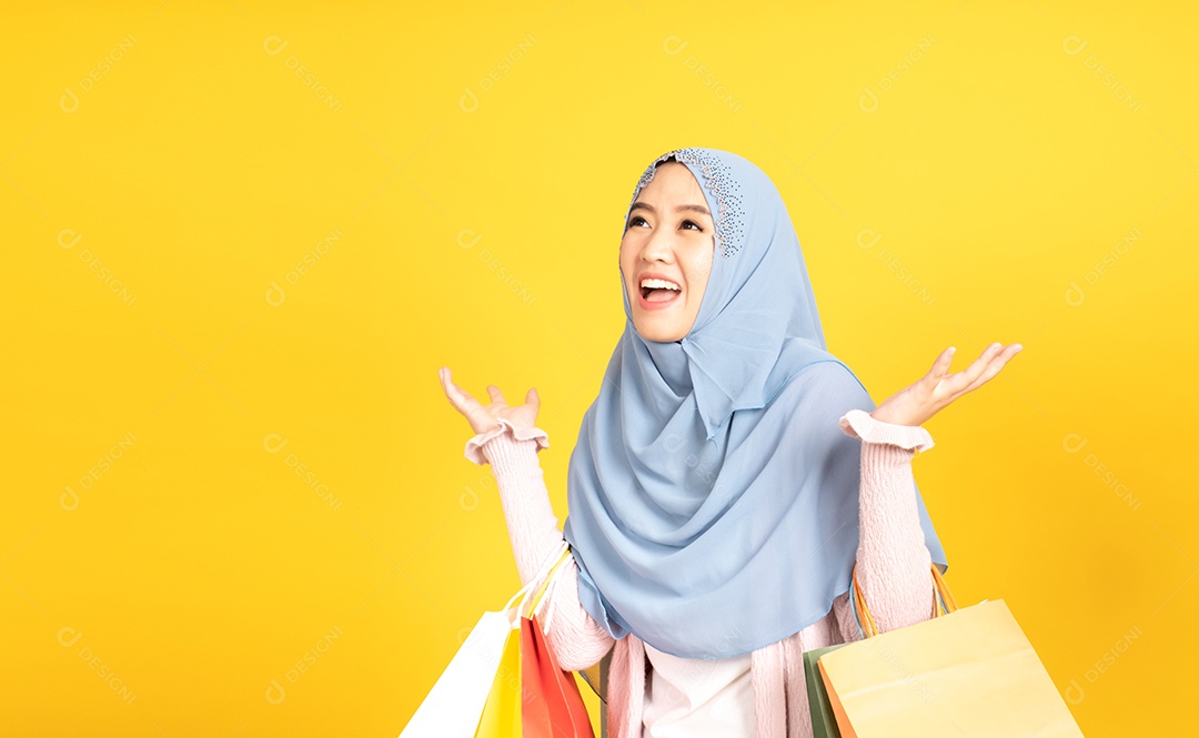 Jovem religiosa árabe sorridente usa hijab de véu segura sacola de compras sobre fundo amarelo.