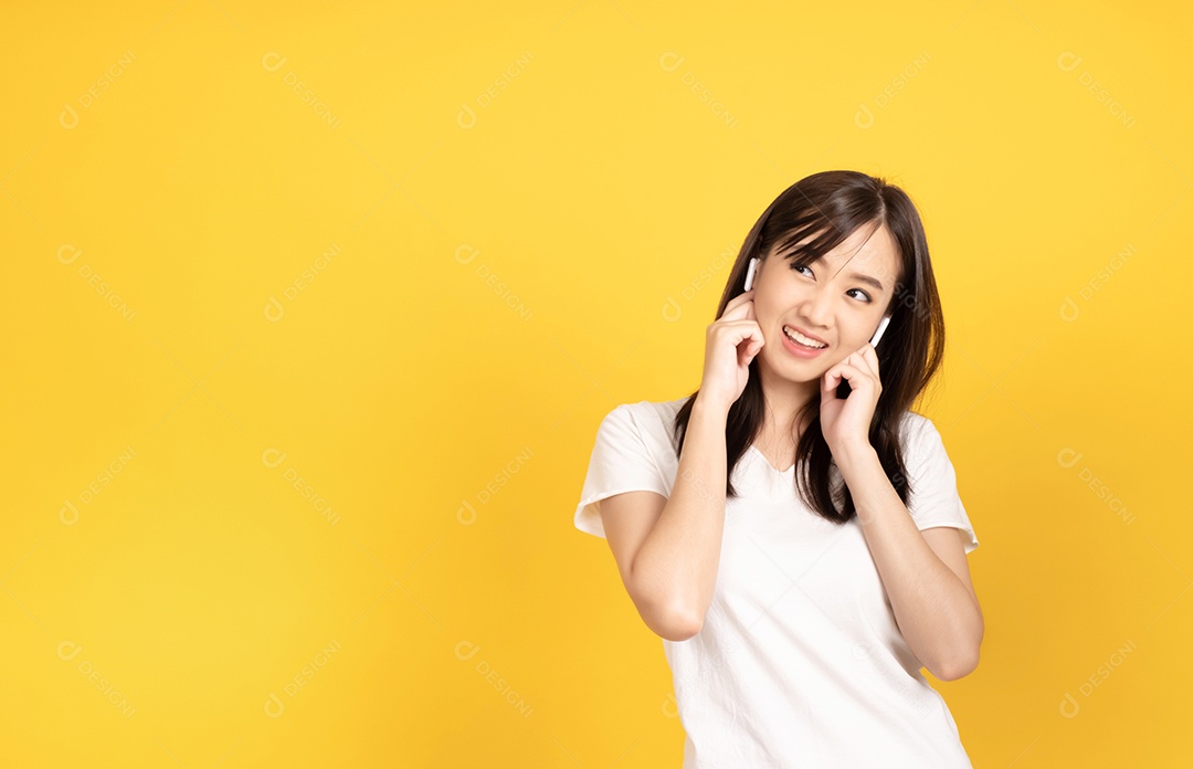 Jovem asiática com fones de ouvido ouvindo música com expressão alegre em fundo amarelo