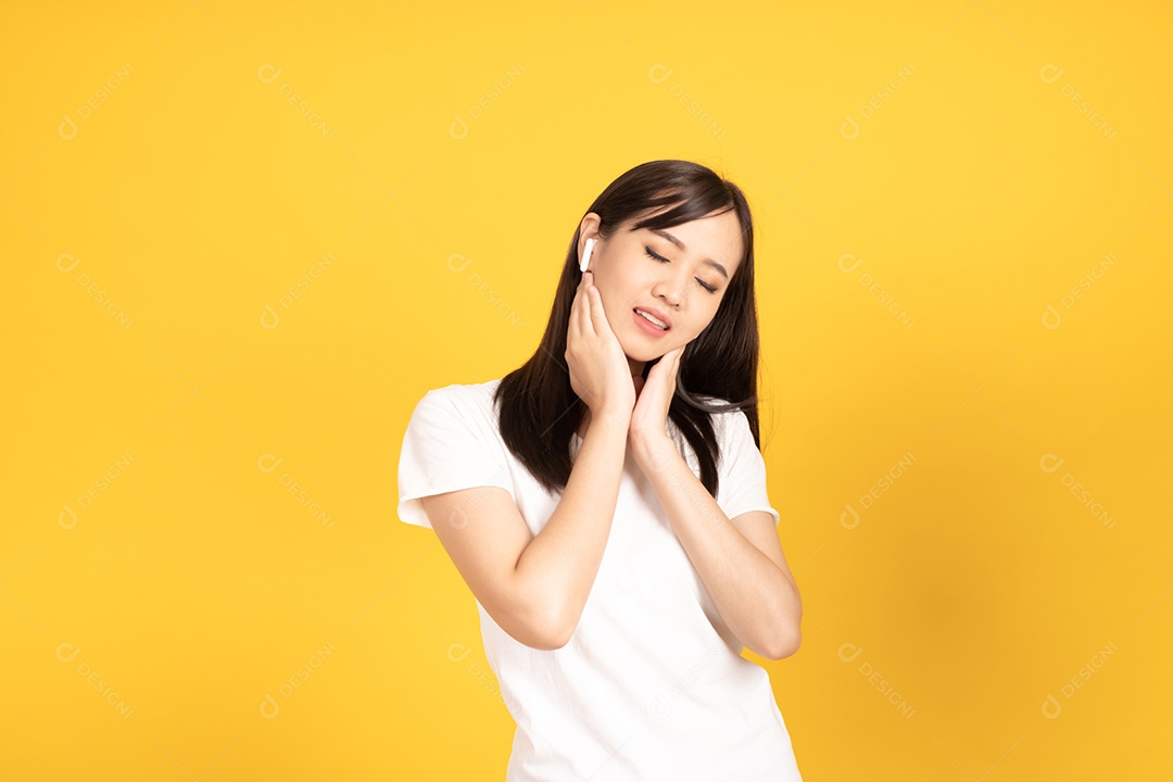 Jovem asiática com fones de ouvido ouvindo música com expressão alegre em fundo amarelo