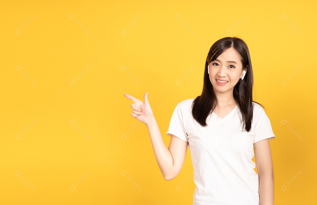 Jovem asiática com fones de ouvido ouvindo música com expressão alegre em fundo amarelo