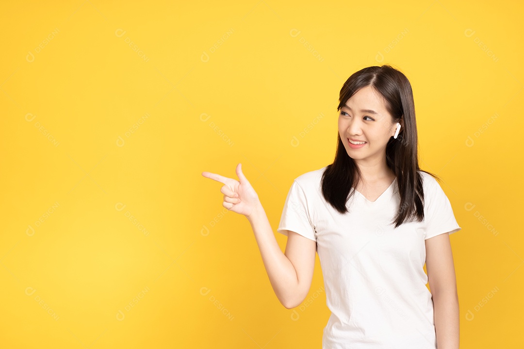 Jovem asiática com fones de ouvido ouvindo música com expressão alegre em fundo amarelo