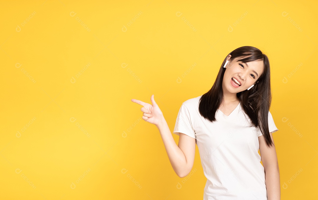 Jovem asiática com fones de ouvido ouvindo música com expressão alegre em fundo amarelo