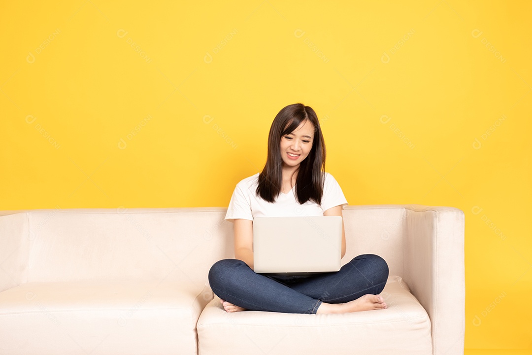 Jovem mulher asiática relaxando no sofá confortável, usando laptop em casa