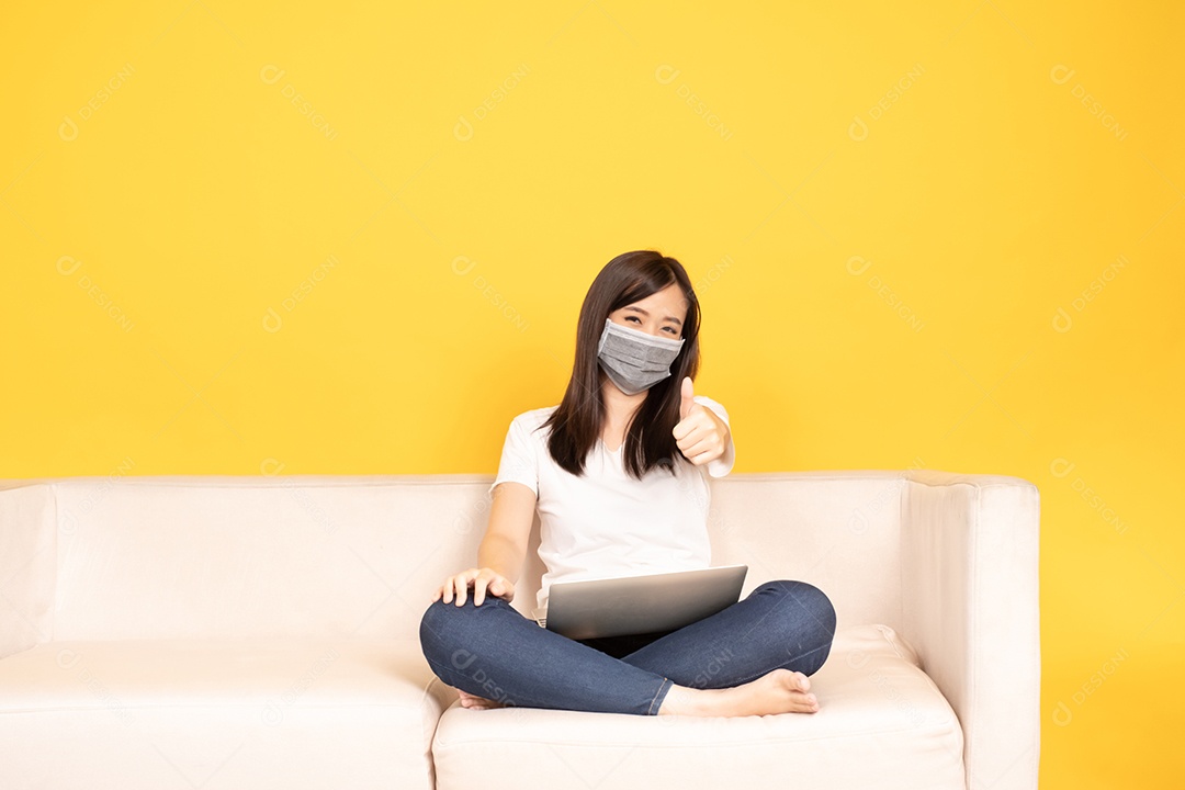 A jovem asiática aponta o dedo no sofá confortável, usando o laptop em casa.