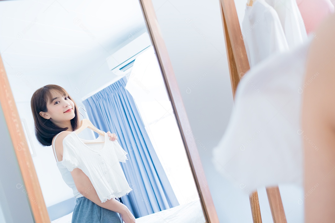 Mulher asiática escolhendo roupas em frente ao espelho