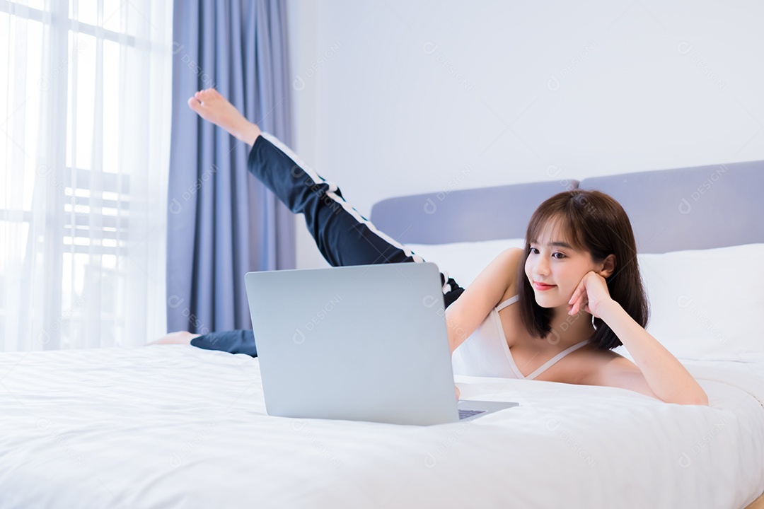 Jovem mulher asiática se exercitando na cama e assistindo aula tutorial online no computador portátil em casa.