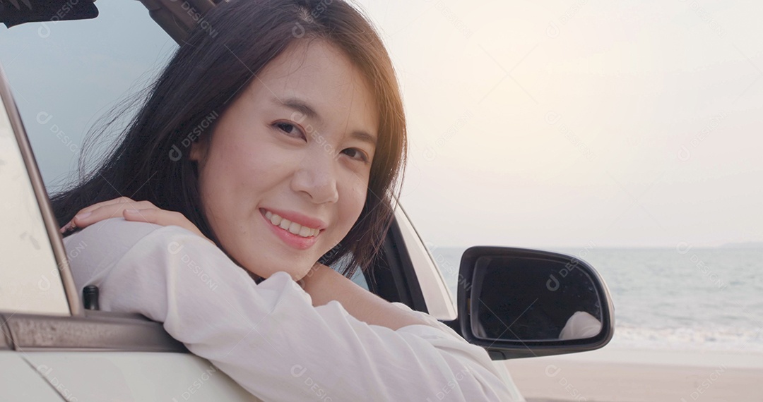Retrato feliz sorrindo de jovem asiática com carro dirigindo na praia