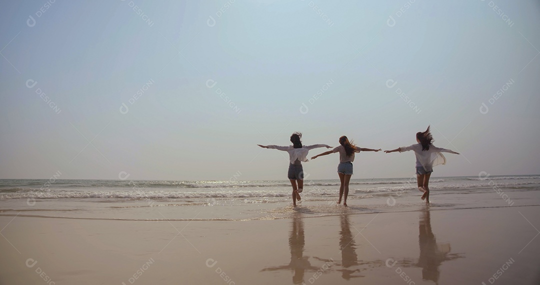 Sorrindo, amigos asiáticos felizes, mulheres correndo e pulando juntos à beira-mar na praia