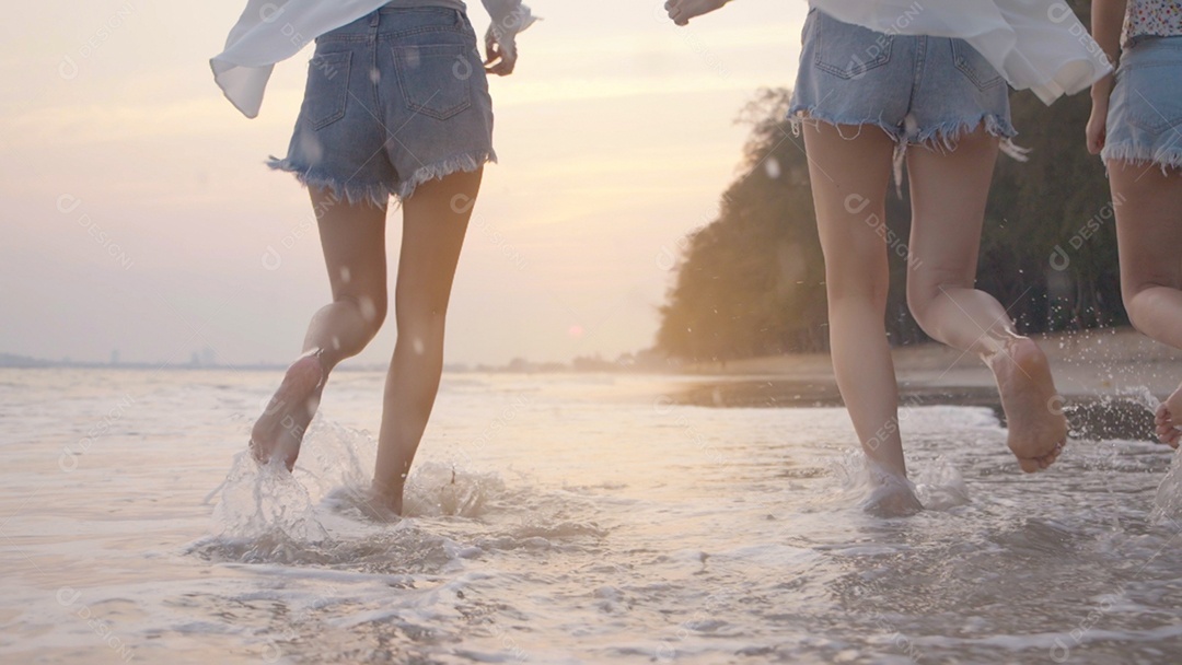 Sorrindo, amigos asiáticos felizes, mulheres correndo e pulando juntos à beira-mar na praia