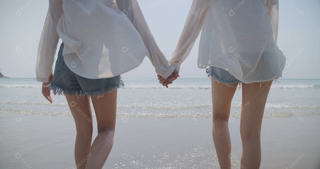 Grupo de melhores amigas jovens de mãos dadas caminhando na praia