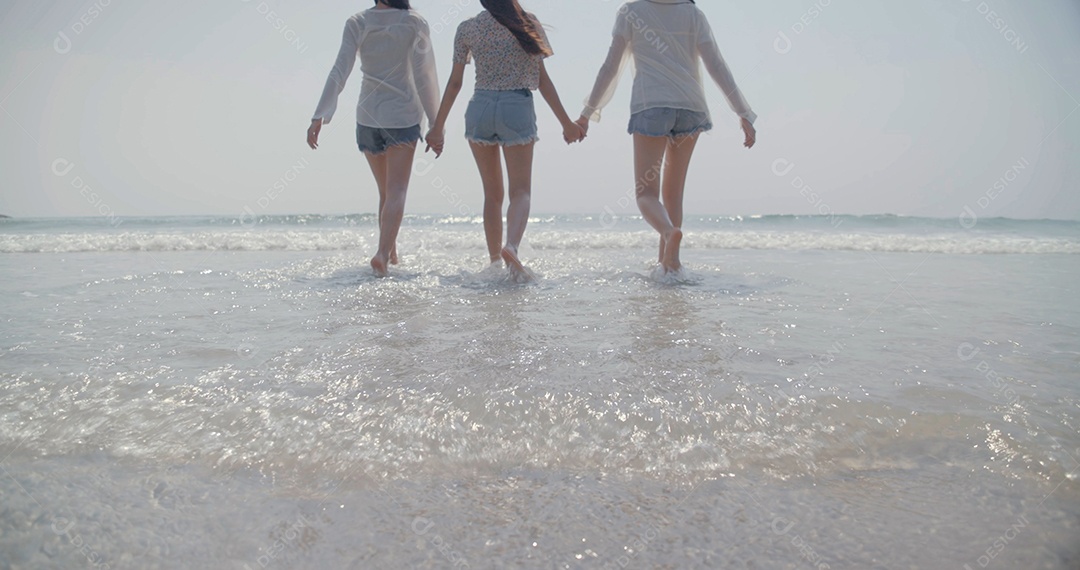 Grupo de melhores amigas jovens de mãos dadas caminhando na praia
