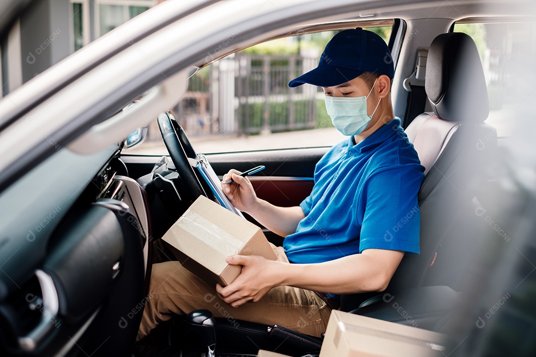 O entregador asiático usando máscara pegando o pacote no transporte para entregas