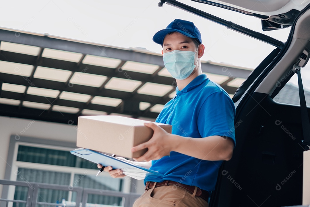 O entregador asiático usando máscara pegando o pacote para a remessa do receptor de casa