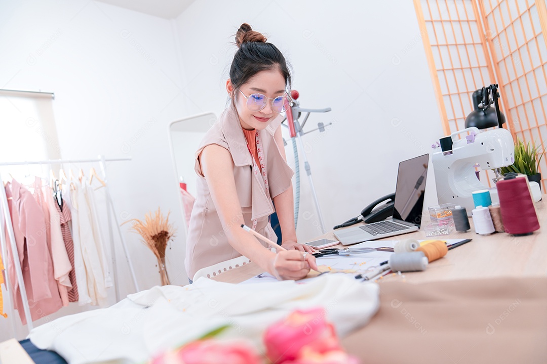Linda estilista de moda asiática trabalhando e costurando suas roupas