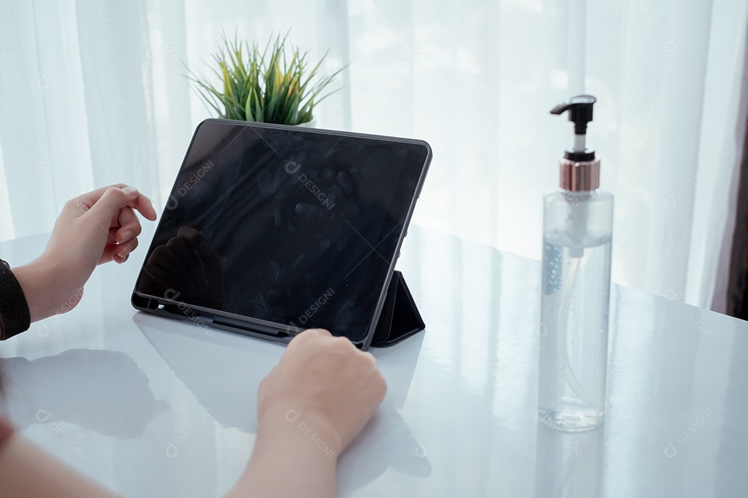 Mulher trabalhando pelo tablet digital com frasco de álcool em gel