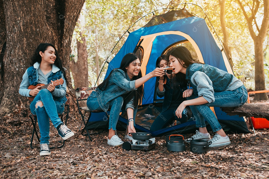 Grupo de jovens mulheres asiáticas acampando e descansando na floresta tocando ukulele