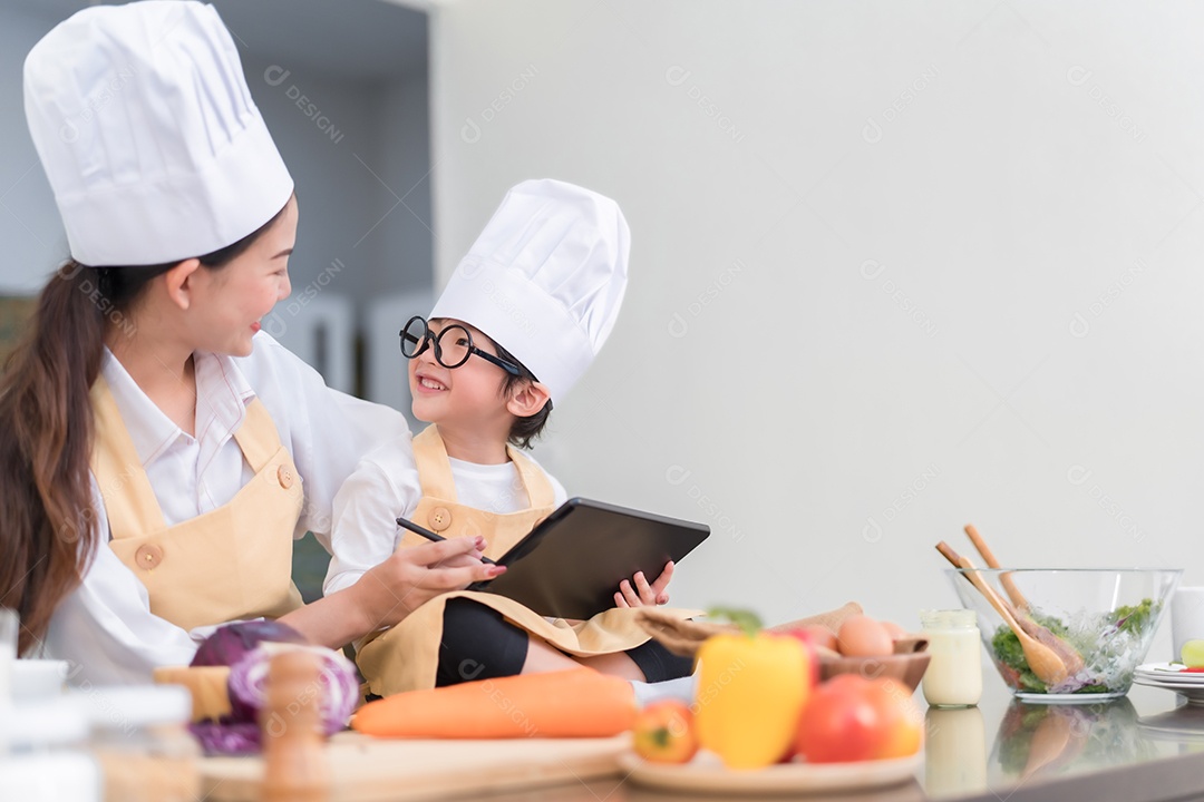 Chef profissional mãe asiática ensinando menu de lista de filho pequeno cozinhando vegetais