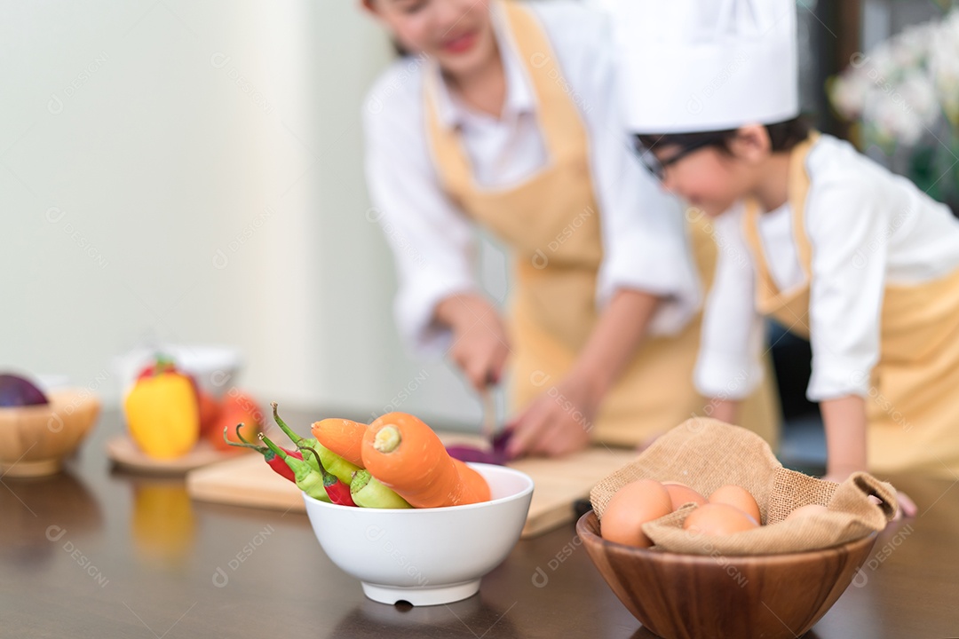 A mãe asiática do chef profissional ensinando o filho pequeno a cozinhar vegetais para salada