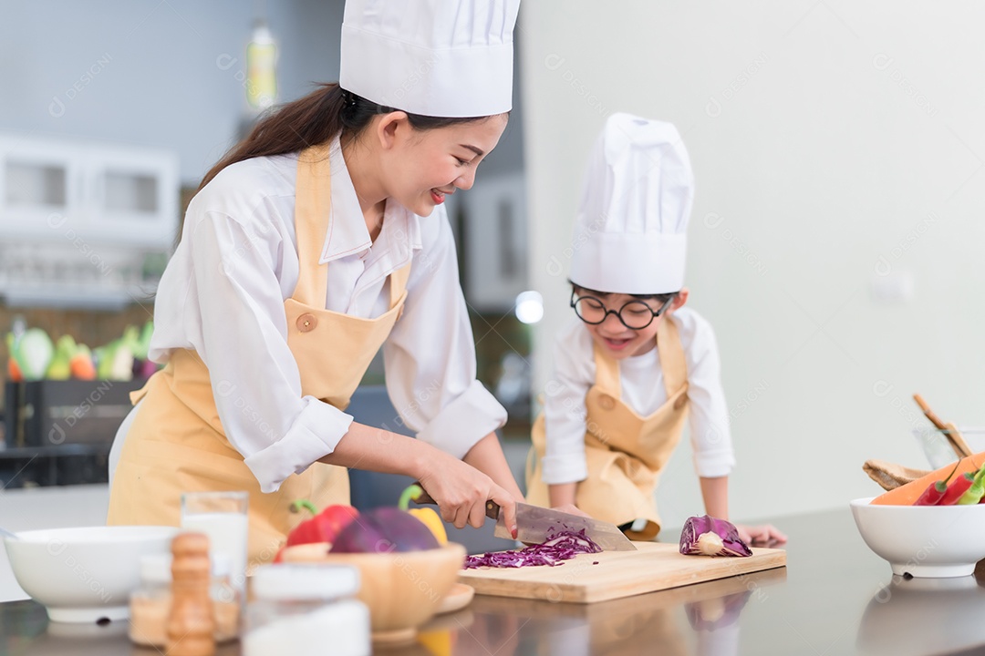 A mãe asiática do chef profissional ensinando o filho pequeno a cozinhar vegetais para salada