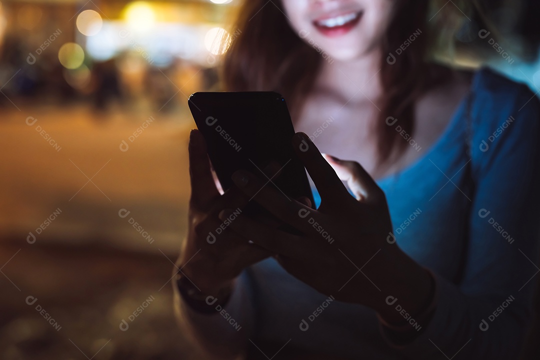 Mulher de beleza olhando smartphone celular à noite na rua