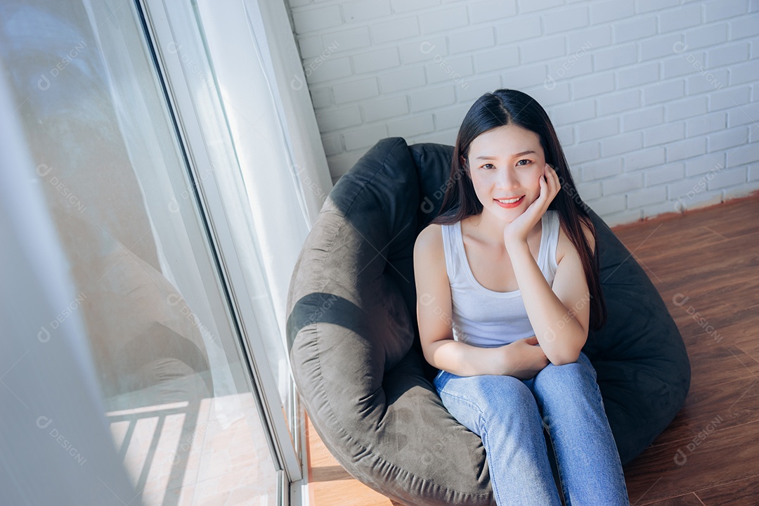Linda mulher asiática sentada no sofá preto relaxa em casa