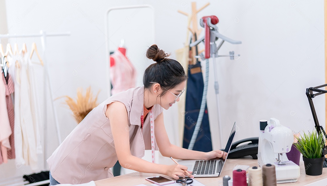 Linda estilista de moda asiática trabalhando e costurando suas roupas de serviço para o cliente