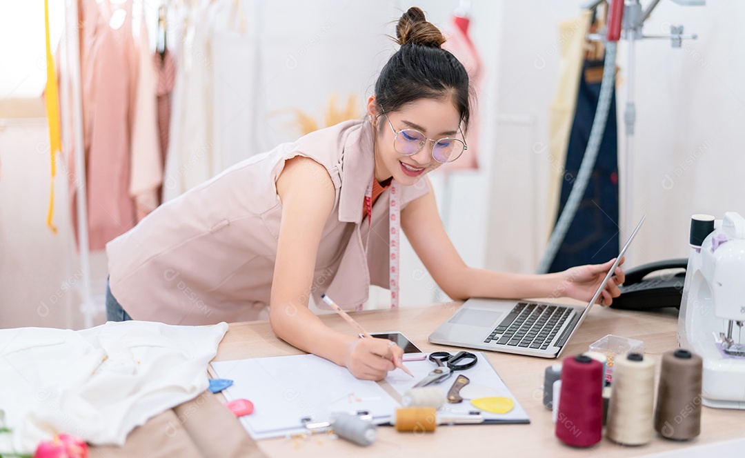 Linda estilista de moda asiática trabalhando e costurando suas roupas de serviço para o cliente