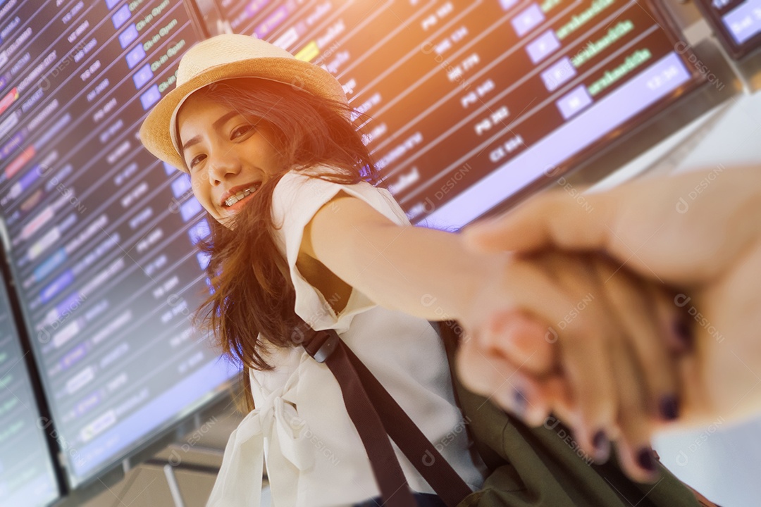 Mulher de mãos dadas namorado caminhando para o quadro de informações no aeroporto