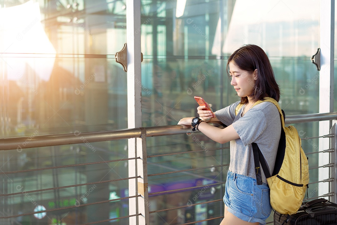 Viajante asiático jovem usando smartphone móvel com bagagem no aeroporto