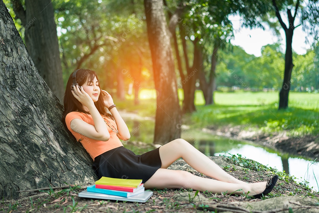Jovem ouvindo música com fone de ouvido e livro feliz relaxa no parque