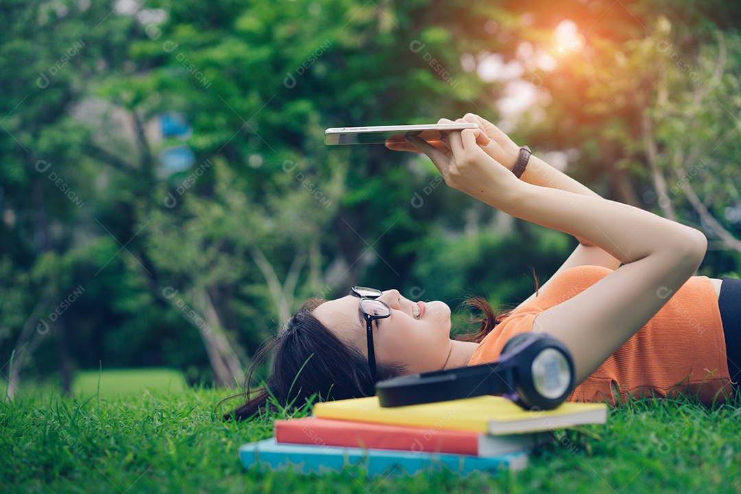 Jovem asiática usando tablet com fone de ouvido e livro