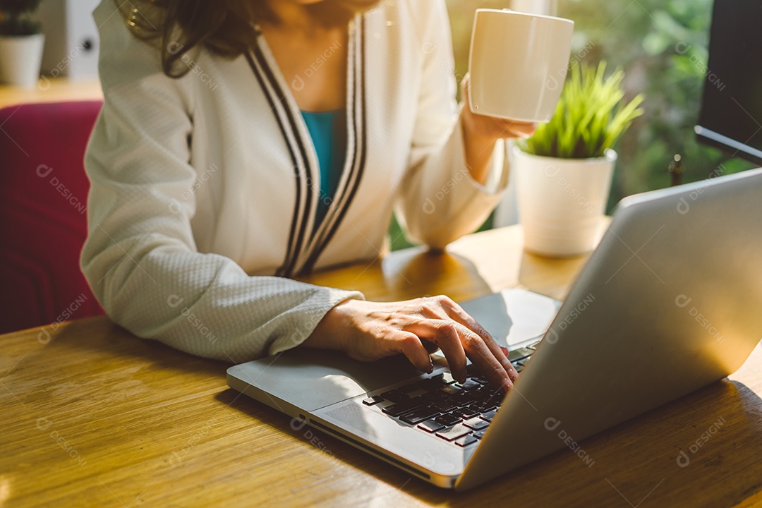 Empresária trabalhando com computador portátil e bebendo coffee break da xícara