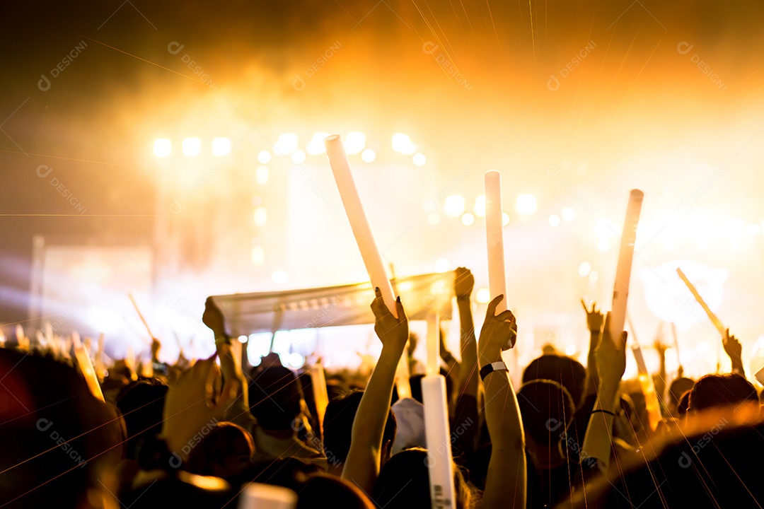 Pessoas levantando as mãos ou bastão luminoso segurando na visão traseira do festival de música