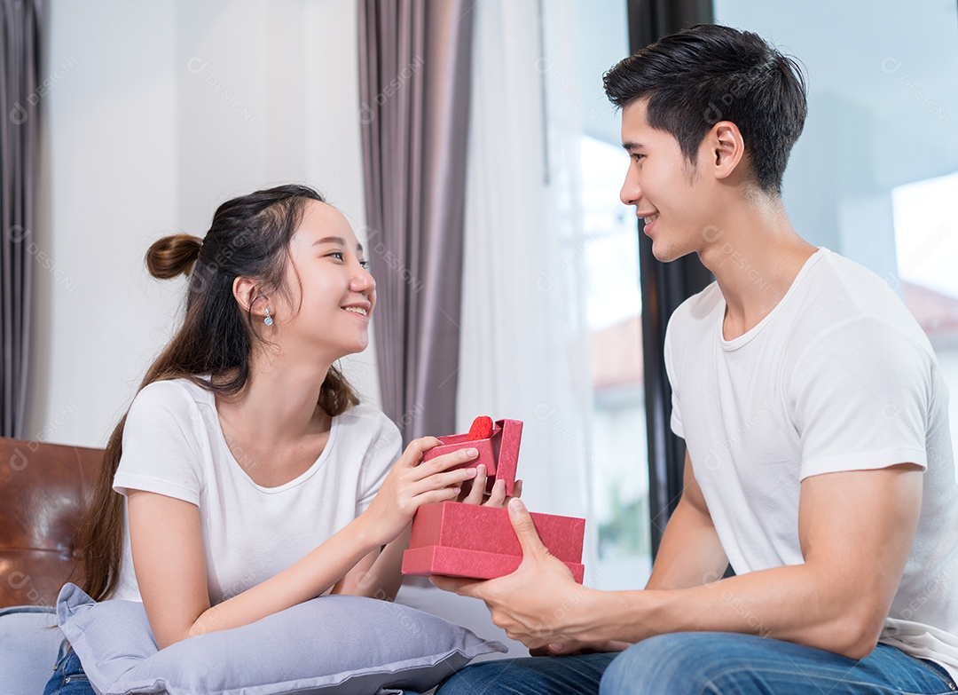 Homem segurando presente de caixa surpresa para mulher no sofá em casa