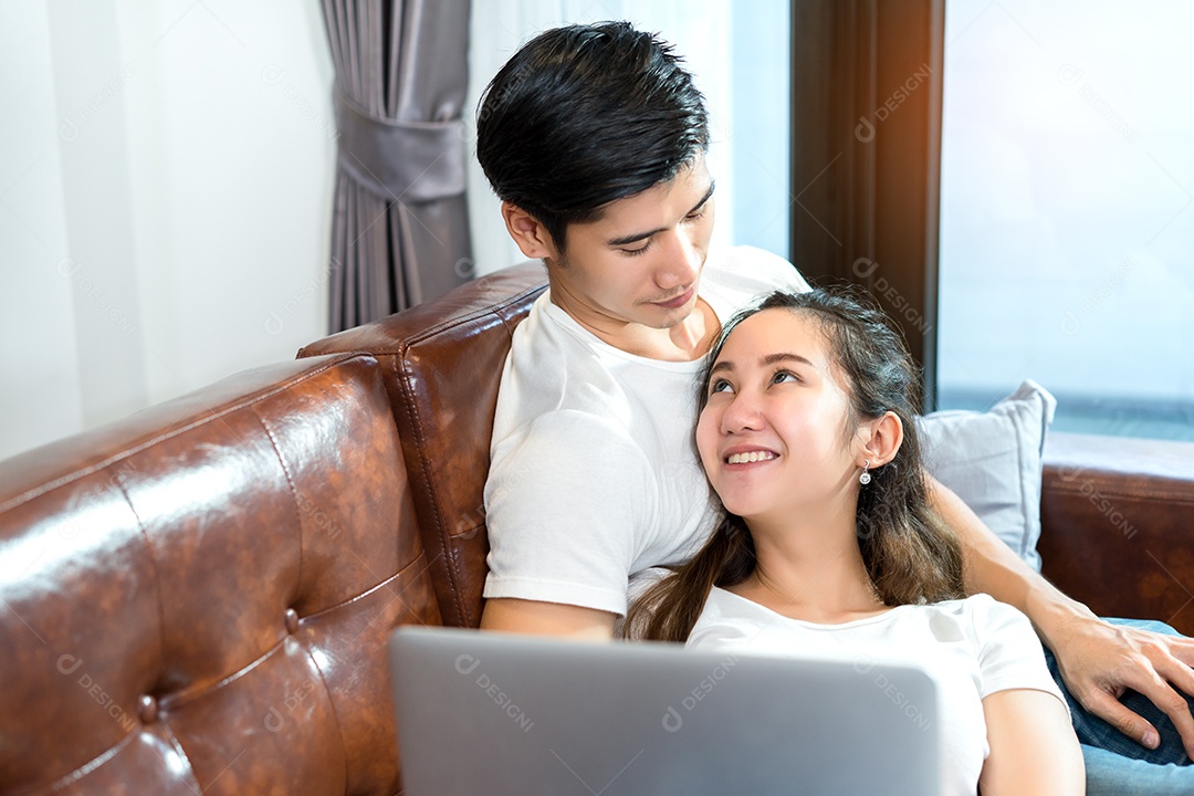 Jovem casal juntos, homem e mulher, olhando o computador portátil feliz e sorrindo relaxando no sofá