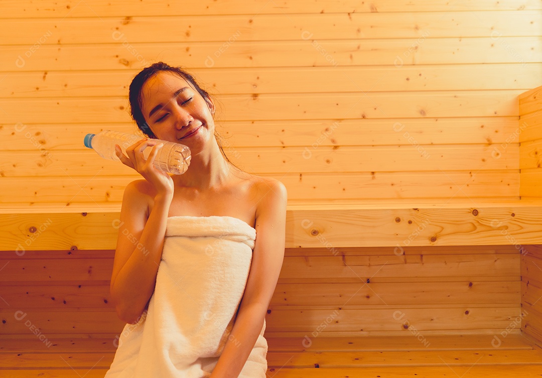 Jovem mulher asiática na sala de spa de sauna com vapor quente segurando garrafa de água feliz relaxando