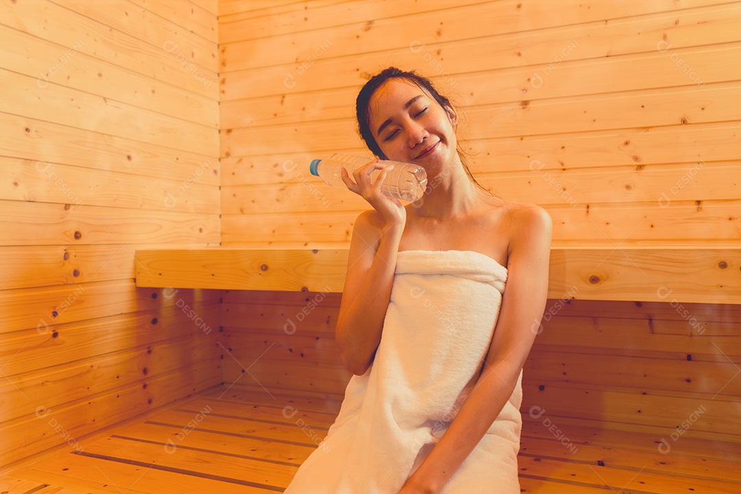 Jovem mulher asiática na sala de spa de sauna com vapor quente segurando garrafa de água feliz relaxando
