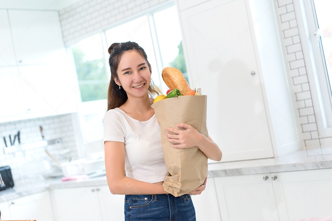 Jovem mulher bonita asiática segura saco de papel de compras com legumes, frutas e pão