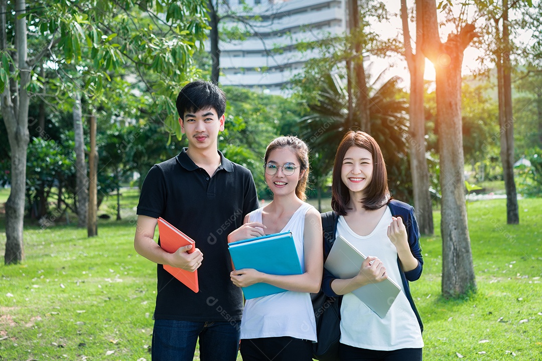 Grupo de jovens estudantes asiáticos com pastas escolares na grama na faculdade