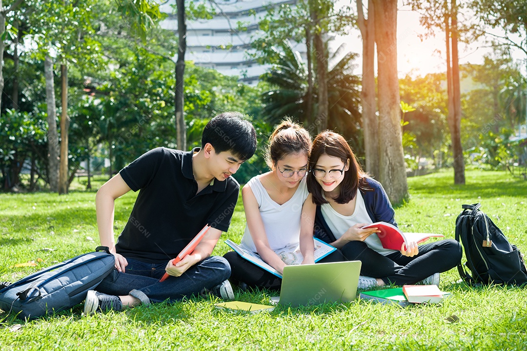 Grupo de jovens estudantes asiáticos com pastas escolares na grama na faculdade