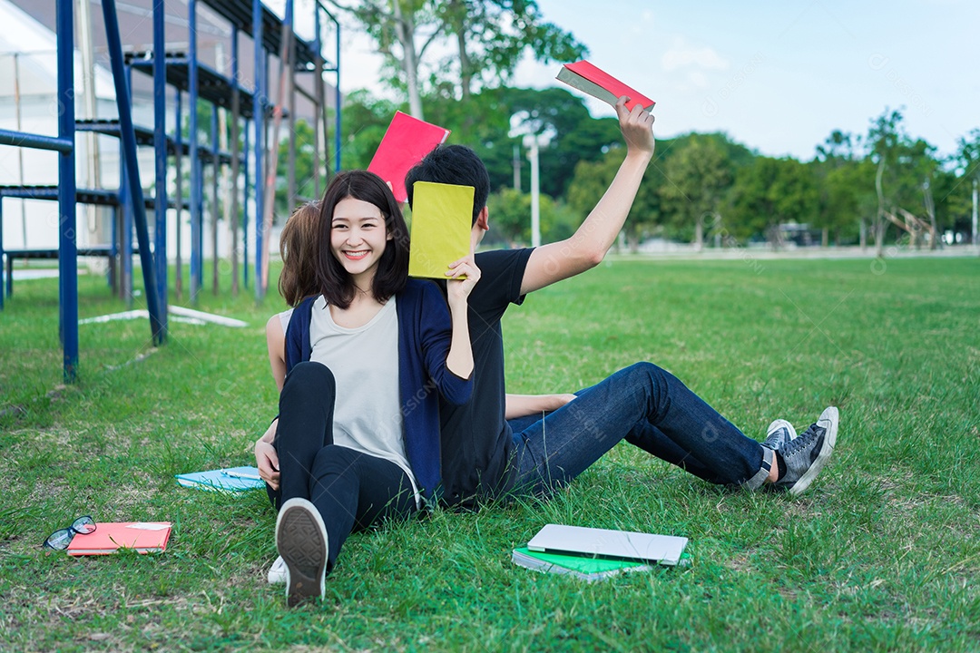 Jovens estudantes juntos sentados na grama abrem pastas escolares e usando computador portátil